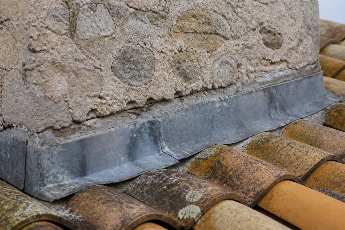 Solin de zinc patiné au pied d&rsquo;une souche de cheminée sur une toiture de tuile canal à La Rochelle